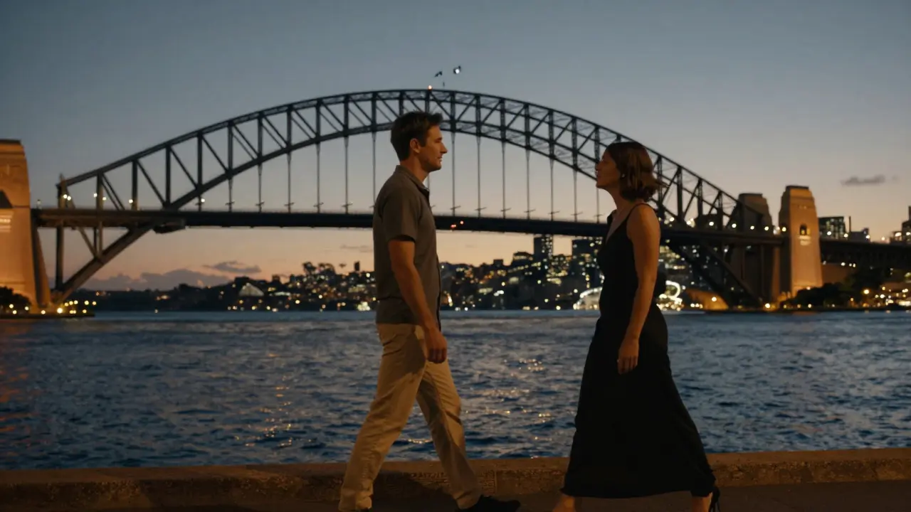 Two people walk peacefully along Sydney Harbour at dusk, chatting quietly under glowing city lights.